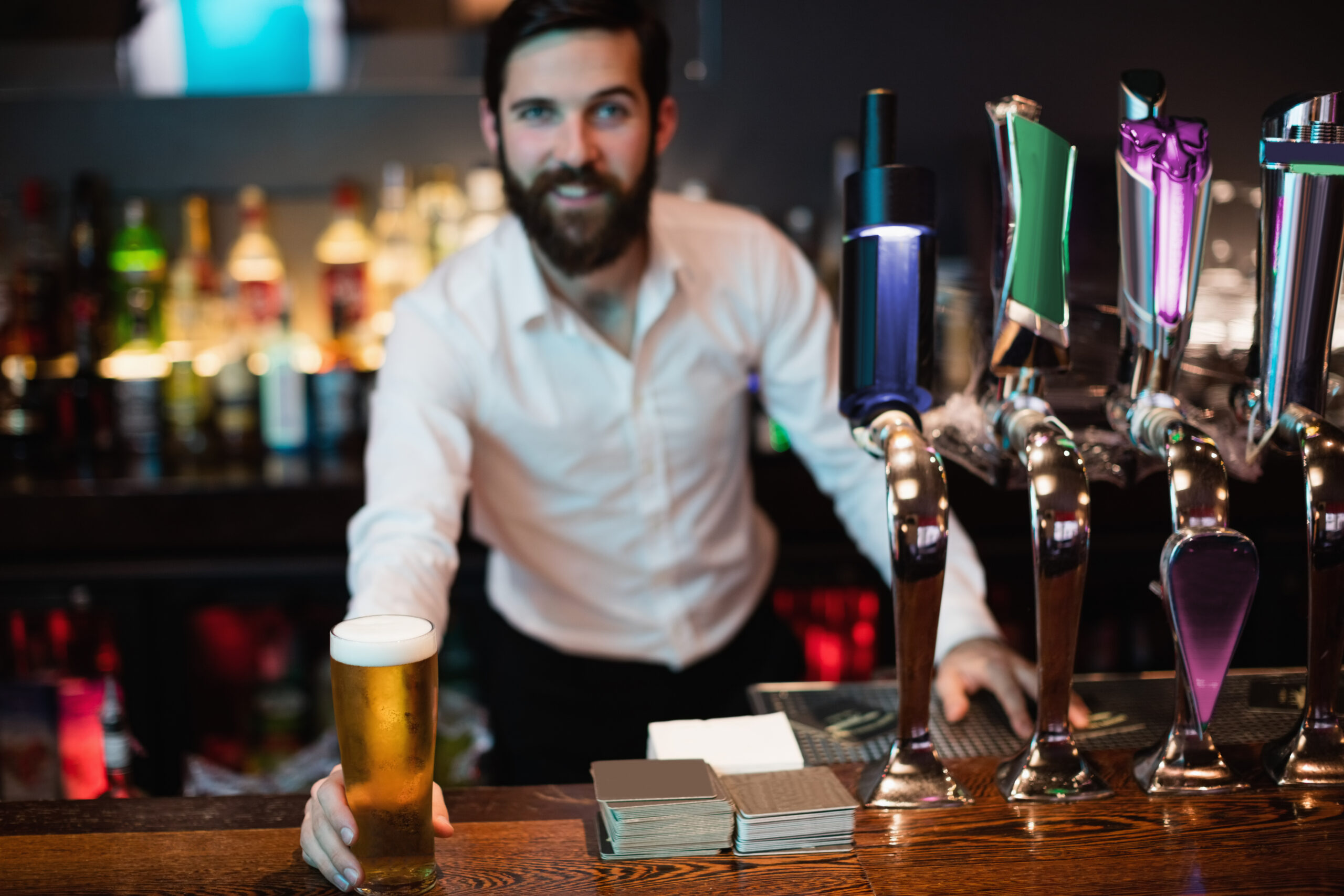 Portrait of bartender holding glass of beer at bar counter